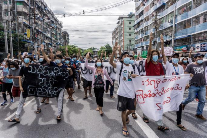 Protesters hold banners while making the three-finger salute during a flash mob demonstration against the military coup in Yangon on June 13, 2021. STR / AFP