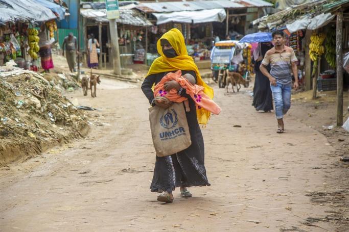 A Rohingya refugee mother with her baby walk on a road along a makeshift camp in Kutubpalang, Ukhiya Cox Bazar district, Bangladesh, 24 August 2022. Photo: EPA