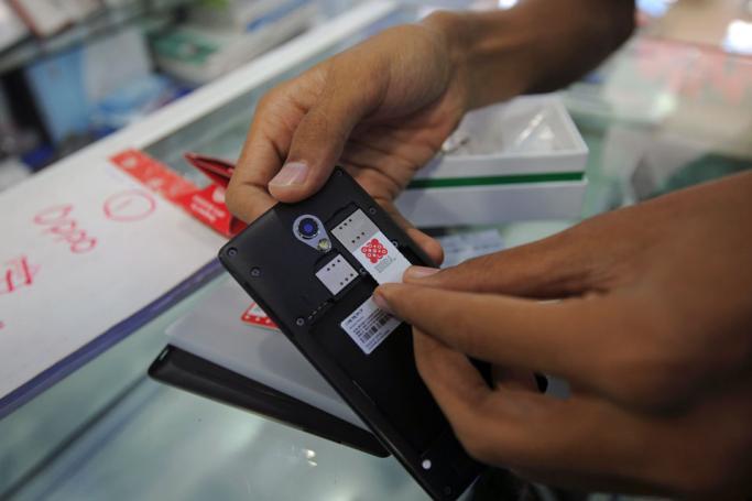 A mobile phone salesman puts an Ooredoo SIM card into a new handset for a customer at a mobile phone shop in Yangon. Photo: AFP