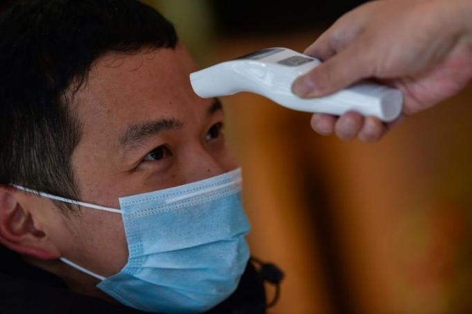 A hotel employee takes the temperature of a man who just arrived in the building in Wuhan (AFP Photo/Hector RETAMAL)