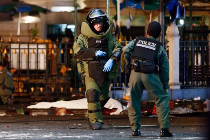 A member of the bomb squad in protective suit talks to a colleague as the body of a victim is seen on the background after an explosion near Erawan Shrine, central Bangkok, Thailand, 17 August 2015. Photo: Rungroj Yongrit/EPA
