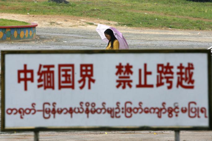 A Burmese woman walks hehind a warning sign standed along the boundary line in the China-Myanmar border town of Wanding, in China's southwestern province of Yunnan. Photo: AFP

