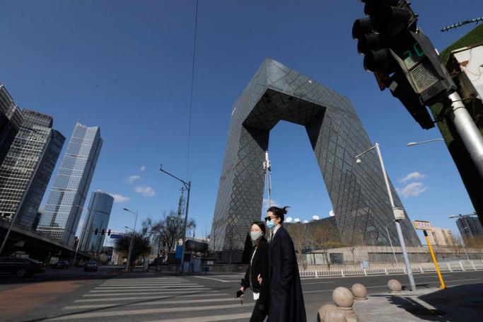 People wearing masks walk near the China Central Television (CCTV) building in the central business district (CBD) in Beijing, China, 14 March 2020. Photo: EPA