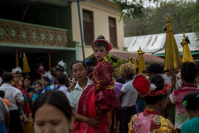 In this photo taken on March 30, 2017, a boy dressed in ornate costume is carried by his father during a parade through town which is part of a ceremony where novice-to-be monks and nuns are inducted into a monastery or nunnery order in the village of Myinkabar. Photo: Ye Aung Thu/AFP
