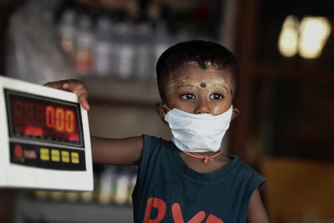 A boy, wearing a face mask as a preventive measure against the COVID-19 novel coronavirus, holds onto an electronic weighing machine at a market in Yangon on March 21, 2020. Photo: Ye Aung Thu/AFP