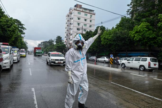 A volunteer wearing personal protective equipment (PPE) directs traffic for ambulances transfering people suspected of having the COVID-19 coronavirus to a quarantine centre in Yangon on October 12, 2020. Photo: Ye Aung Thu/AFP
