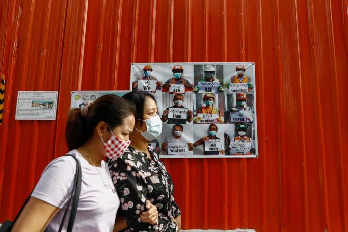 Women wearing protective face masks walks pass near a poster promoting health and education to wear mask amid the ongoing pandemic of the COVID-19 disease caused by the SARS-CoV-2 coronavirus at downtown area in Yangon, Myanmar, 22 July, 2020. Photo: Lynn Bo Bo/EPA
