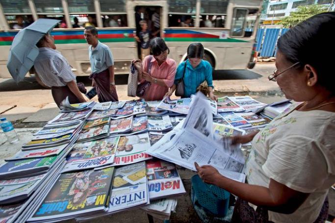 A street vendor reads a new private daily newspaper while selling newspapers and weekly journals at a roadside stall in Yangon, Myanmar, April 1, 2013. Photo: Lynn Bo Bo/EPA
