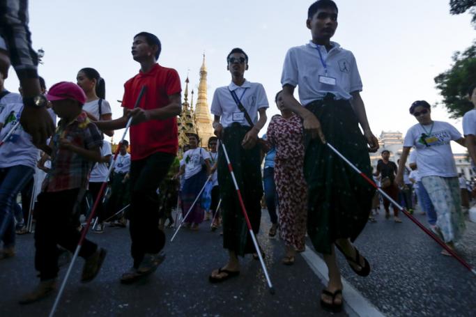 (File) Visually impaired persons and helpers walk pass Sule pagoda as they take part in a rally to mark International White Cane Day, in Yangon, Myanmar, 15 October 2018. Photo: EPA