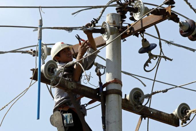 A labourer works on an electric power pole to modify and maintain the high voltage power cables in Mandalay, Myanmar. Photo: EPA