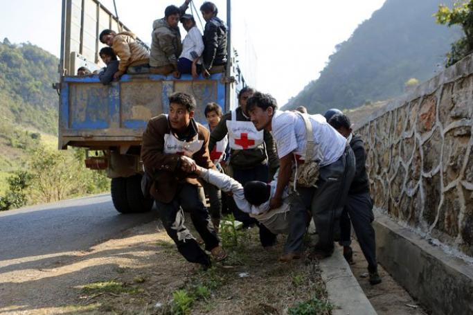 Volunteers of Myanmar Red Cross organisation carry wounded volunteer U Moe Kyaw, 45, as the war vrefugees fleeing from Laukkai sit on the truck after vehicles of a rescue convoy were attacked by Kokang rebels near Kokang capital Laukkai, northern Shan State, Myanmar, February 17, 2015. Two volunteers from Myanmar Red Cross Society injured in rescue convoy attack. Photo: Lynn Bo Bo/EPA
