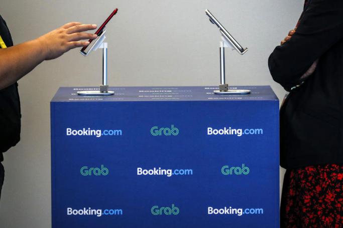 (File) A woman uses a mobile phone displayed on a table with the logos of Booking.com and ride hailing service Grab during a product launch announcement in Singapore, 29 October 2019. Photo: WALLACE WOON/EPA