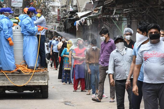Municipal workers spray disinfectant on people standing in a queue next to a Mobile Covid-19 Testing station at a residential area in the old Delhi area, New Delhi, India, 20 April 2020. Photo: EPA