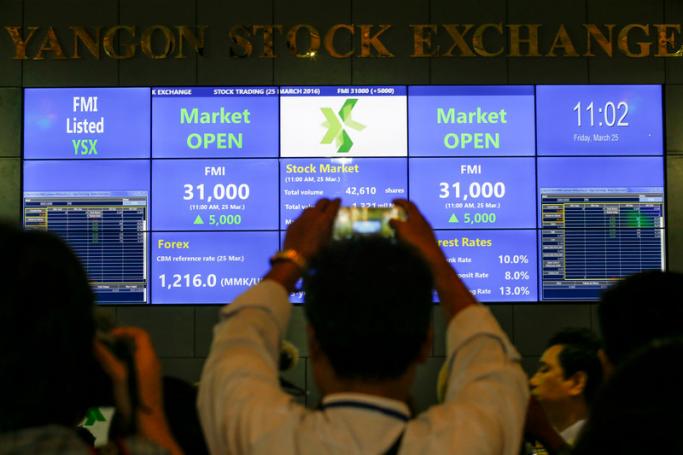 (File) A man takes a photograph of an electronic board showing the FMI (First Myanmar Investment) index at Yangon Stock Exchange, Yangon. Photo: Lynn Bo Bo/EPA