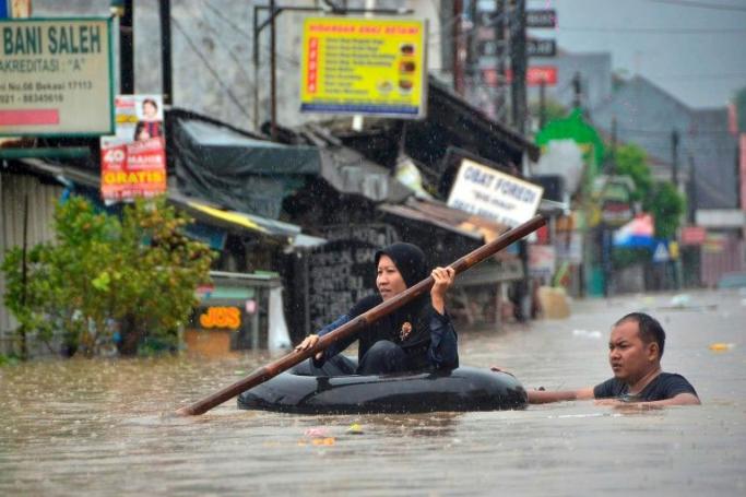 A woman crosses a flooded area in an inflated inner-tube in Bekasi, near Jakarta (AFP Photo/REZAS) 
