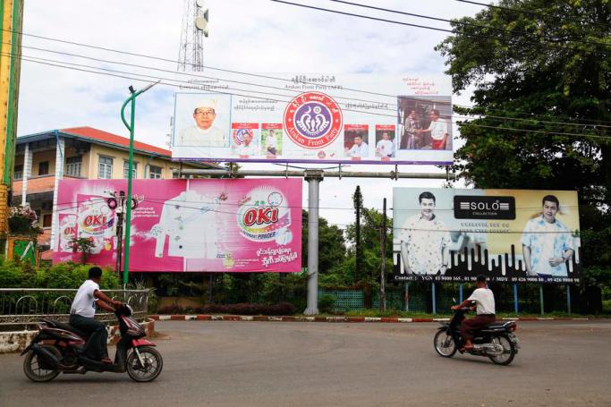 Rakhine people wearing protective face masks travel by motocycle near the campaign billboard for the Arakan Front Party (AFP) in Sittwe, Rakhine State, Myanmar, 17 October 2020. Photo: Nyunt Win/EPA