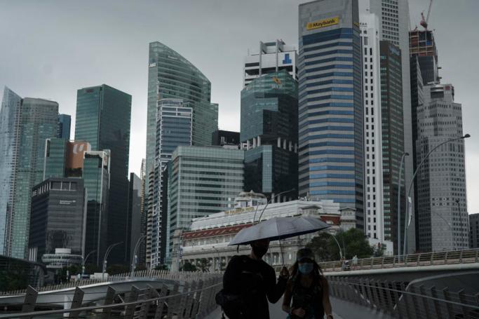 A couple hold an umbrella while crossing a bridge in front of the financial district in Singapore, 22 January 2021. Photo: EPA