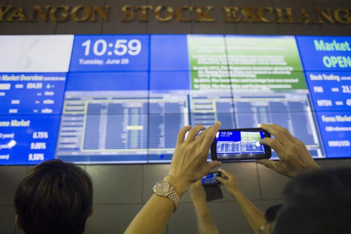 A visitor takes a photo of a large video screen displaying stock prices at the Yangon Stock Exchange in Yangon. Photo: Ye Aung Thu/AFP
