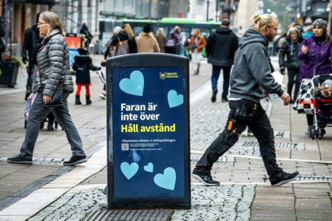 People walk past a trash can with a sign reading "The danger is not over - Keep your distance" in the Swedish city of Uppsala (Photo: AFP)