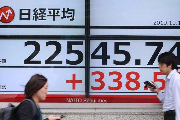Pedestrians walk in front of an electric quotation board displaying the numbers on the Nikkei 225 index on the Tokyo Stock Exchange October 16, 2019. Photo: AFP