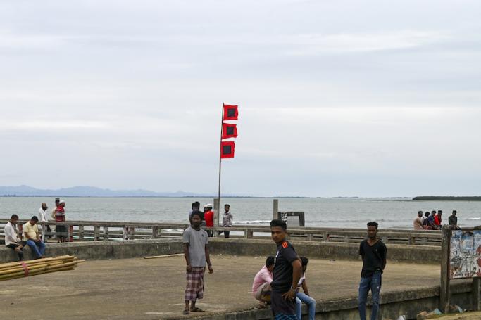 People gather beside a storm danger signal flag in Shahpori island jetty on May 13, 2023, ahead of Cyclone Mocha's landfall. Photo: AFP