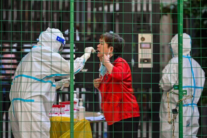 A Health worker takes a swab sample from a woman by the entrance of a residential area under Covid-19 lockdown in the Xuhui district of Shanghai on June 8, 2022. Photo: Hector RETAMAL / AFP 