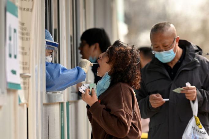 A health worker gets a swab sample from a woman to be tested for Covid-19 coronavirus at a swab collection site in Beijing on March 16, 2022. Photo: AFP