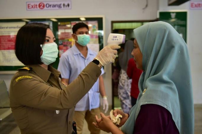 A border officer takes a woman's temperature at a customs checkpoint in Sungai Kolok in southern Thailand on the border with Malaysia on March 15 (AFP Photo/Madaree TOHLALA) 