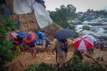 Onlookers stand as Rohingya refugees work amid the debris of houses in Balukhali camp on July 27, 2021 that were damaged after monsoon rains triggered landslides and flash floods in the hilly settlements killing at least six. Photo: Tanbir Miraj/AFP