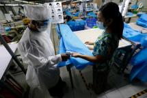  A security person with protective suit sprays hand sanitizer to a worker who makes disposable surgical gown at a garment factory in Yangon, Myanmar, 02 May 2020. Photo: EPA