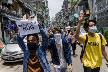 A protester holds a sign in support of the National Unity Government (NUG) as others make the three-finger salute during a demonstration against the military coup in Yangon's Sanchaung township. Photo: AFP