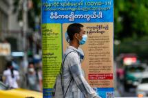 A man wearing a protective face mask passes near a poster promoting health and education about SARS-CoV-2 coronavirus amid the ongoing pandemic of the COVID-19 disease at downtown area in Yangon. Photo: Lynn Bo Bo/EPA