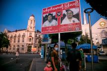 People wearing facemasks wait for a bus under an election campaign poster in Yangon on October 7, 2020. Photo: Sai Aung Main / AFP
