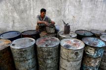 A Myanmar worker fixes the lids of oil barrels near a jetty of Yangon river in Yangon, Myanmar. Photo: EPA