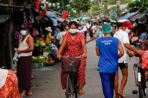 A woman wearing protective face mask drives a bicycle pass a street market in Yangon, Myanmar. Photo: EPA