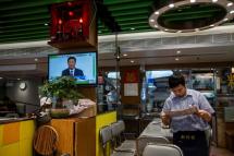 A waiter reads the newspaper as a live broadcast of Chinese President Xi Jinping shows on the television at a Hong Kong eatery in December 2019 (AFP Photo/ISAAC LAWRENCE) 
