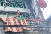 A woman on a balcony in an apartment block in Thinganggyun Township, Yangon, with USDP campaign material bearing the president's image, on Nov. 3. (PHOTO: Myanmar Now/Phyo Thiha Cho) 
